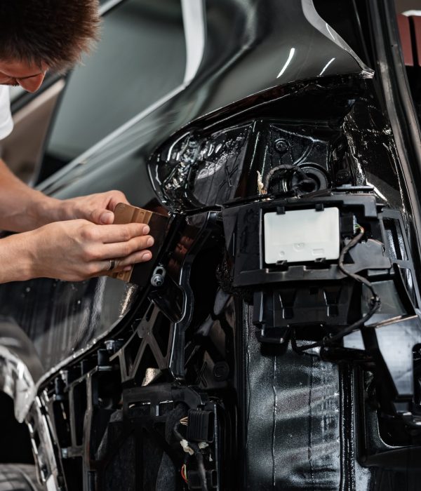 Close up photo of car wrapping specialist putting protective film on a car in detailing service