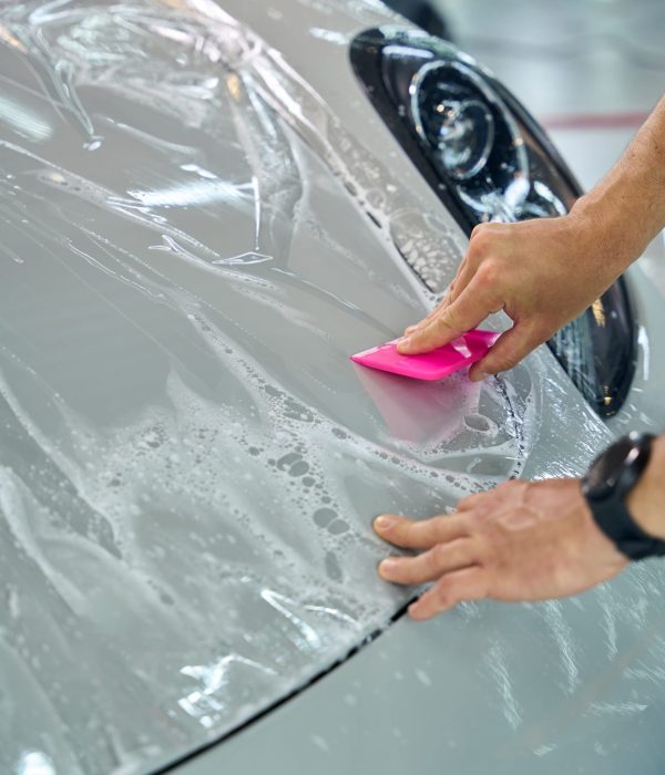 Master uses special spatula to apply a protective film to the body of a car, he works with modern cars