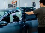 a car mechanic carefully sticks a protective tinted film on a car glass at detailing station