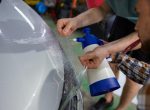 Closeup concentrated man worker smoothing protective vinyl film in garage. Car detailing and maintenance